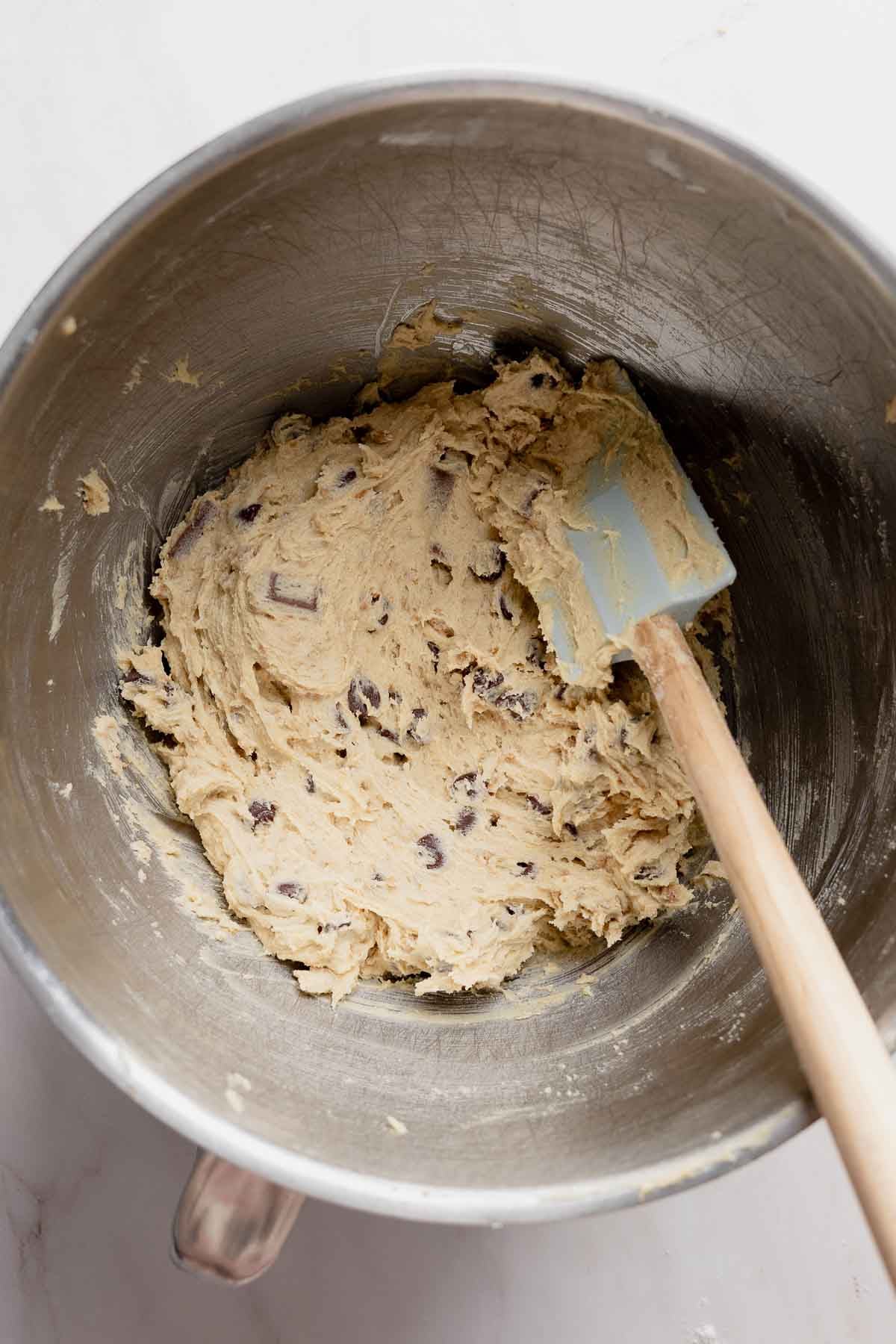 Cookie dough mixed in a stand mixer bowl, spatula resting inside the bowl.