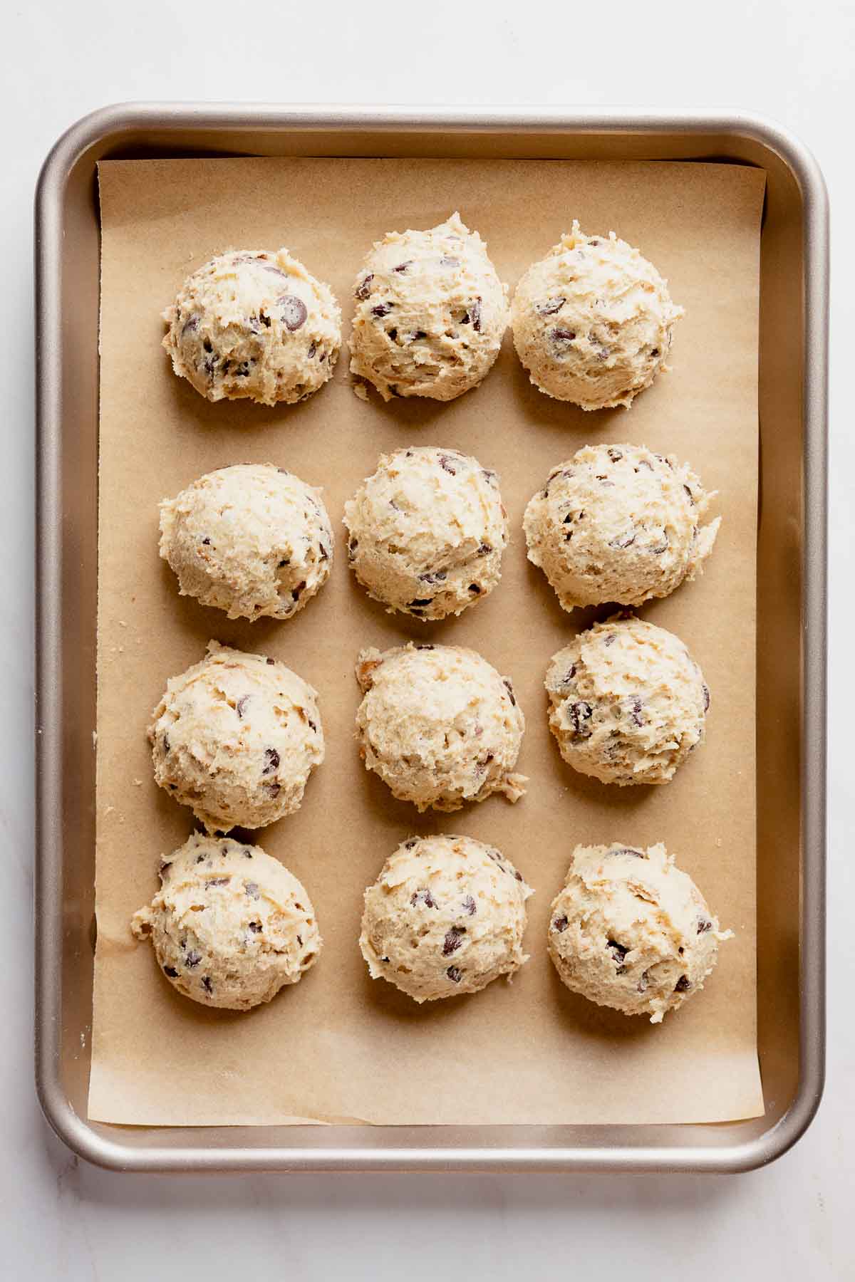 Cookie dough portioned into twelve mounds, placed on parchment lined baking sheet.