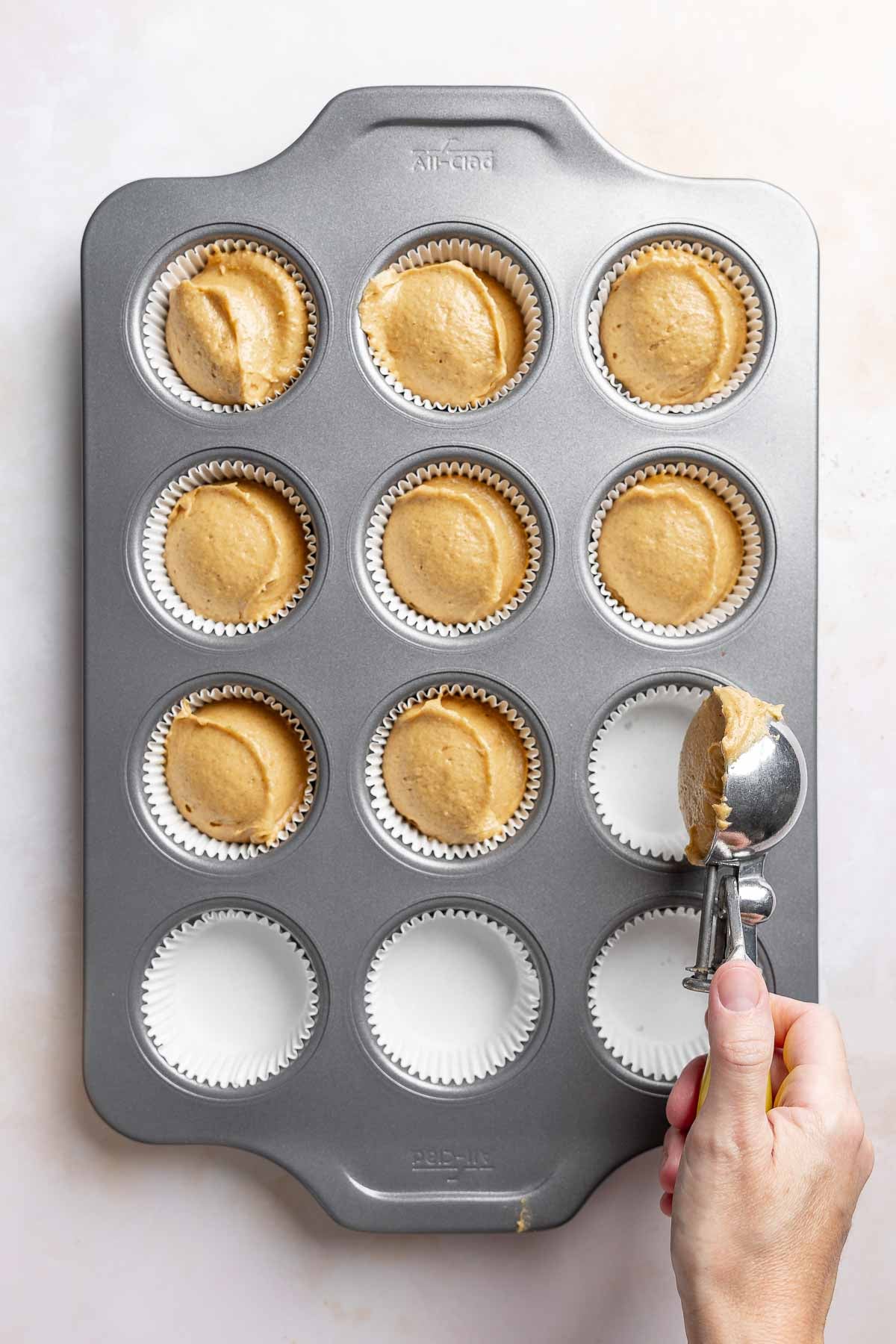 Scooping muffin batter into muffin tin lined with paper baking cups.