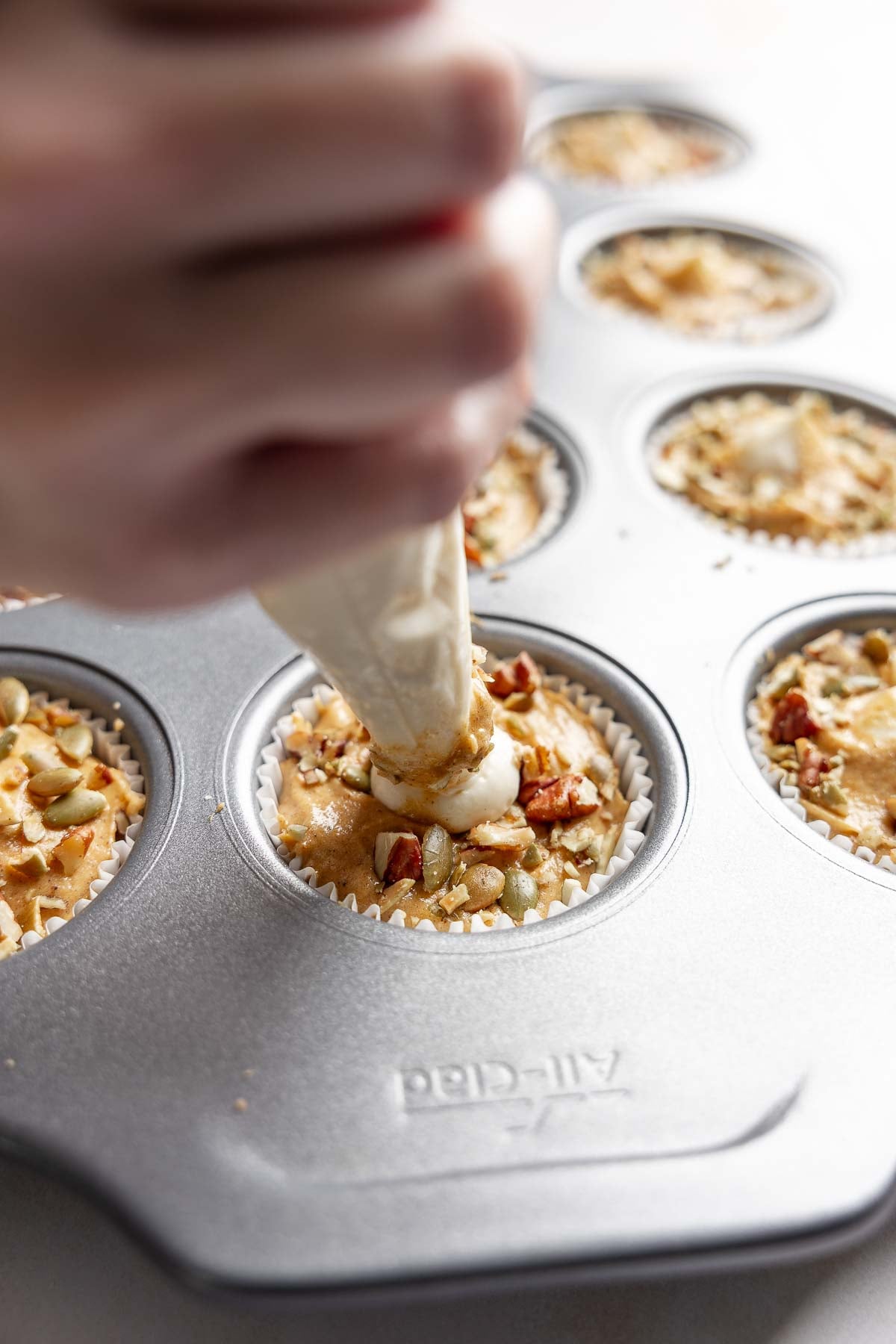 Piping bag filling center of muffin batter with cream cheese filling.