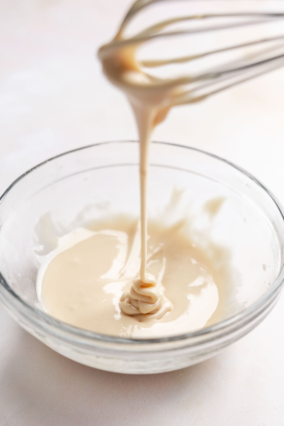 Maple glaze dripping from whisk into bowl.
