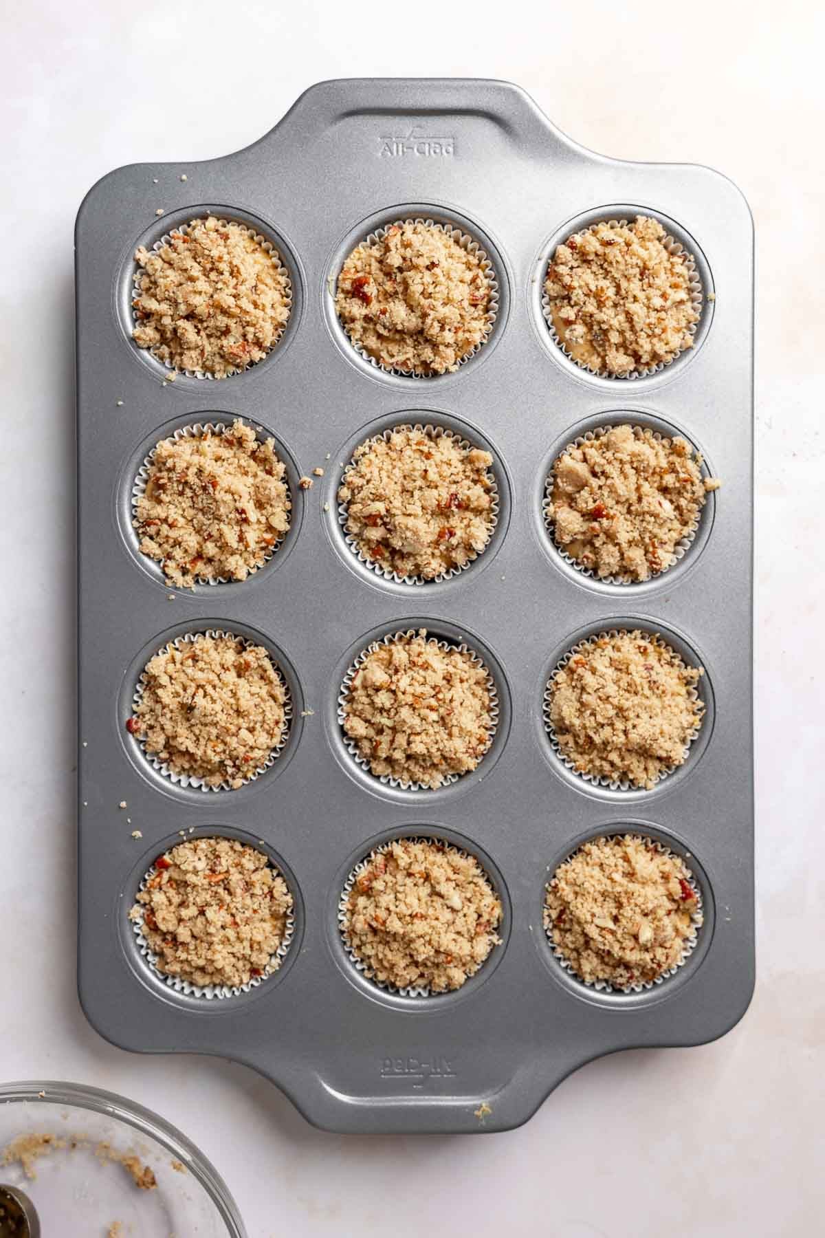 Muffin batter in muffin pan topped with streusel, ready to bake.