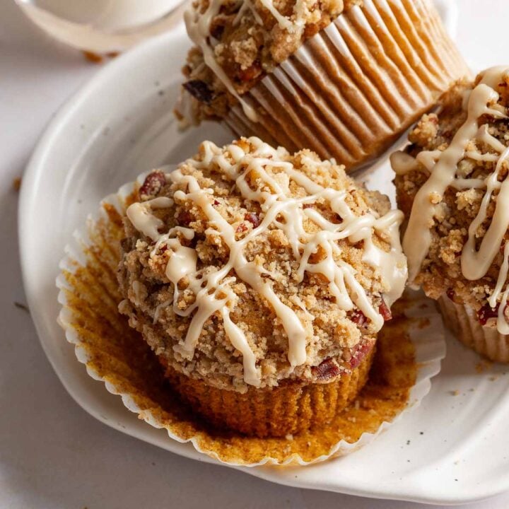 Three gluten-free pumpkin muffins on a plate, one with wrapper peeled back to show texture.