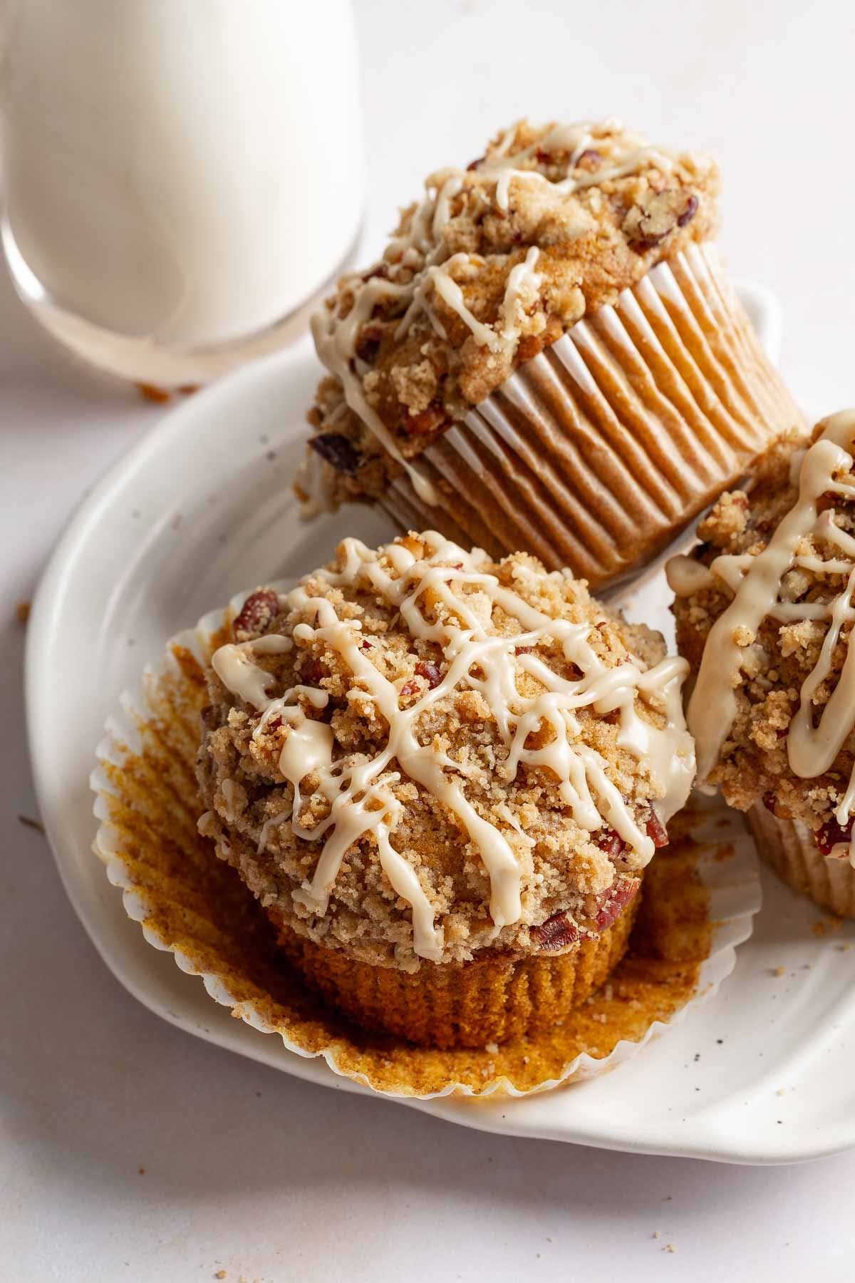 Three gluten-free pumpkin muffins on a plate, one with wrapper peeled back to show texture.