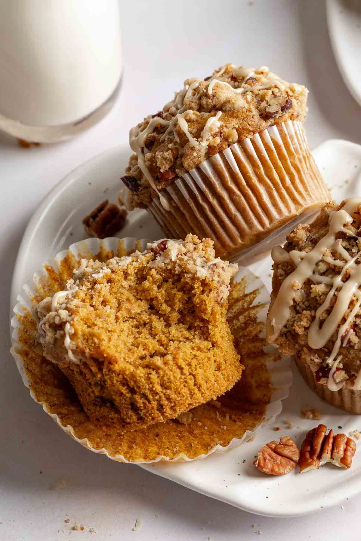 Gluten-free pumpkin streusel muffins on a pumpkin shaped plate, one with bite taken to show soft texture.