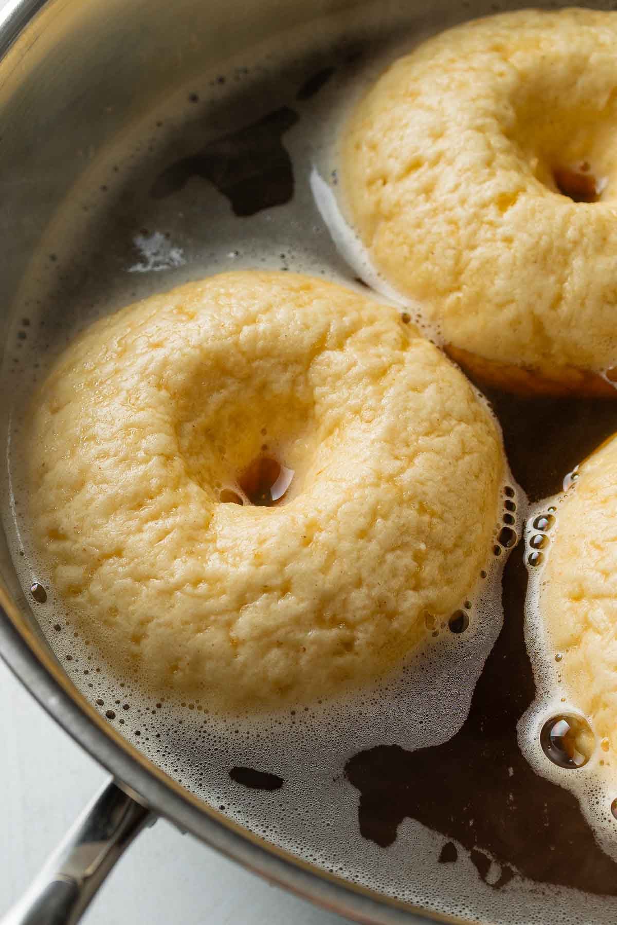 Bagels floating in a pan of boiling water with molasses and baking soda.