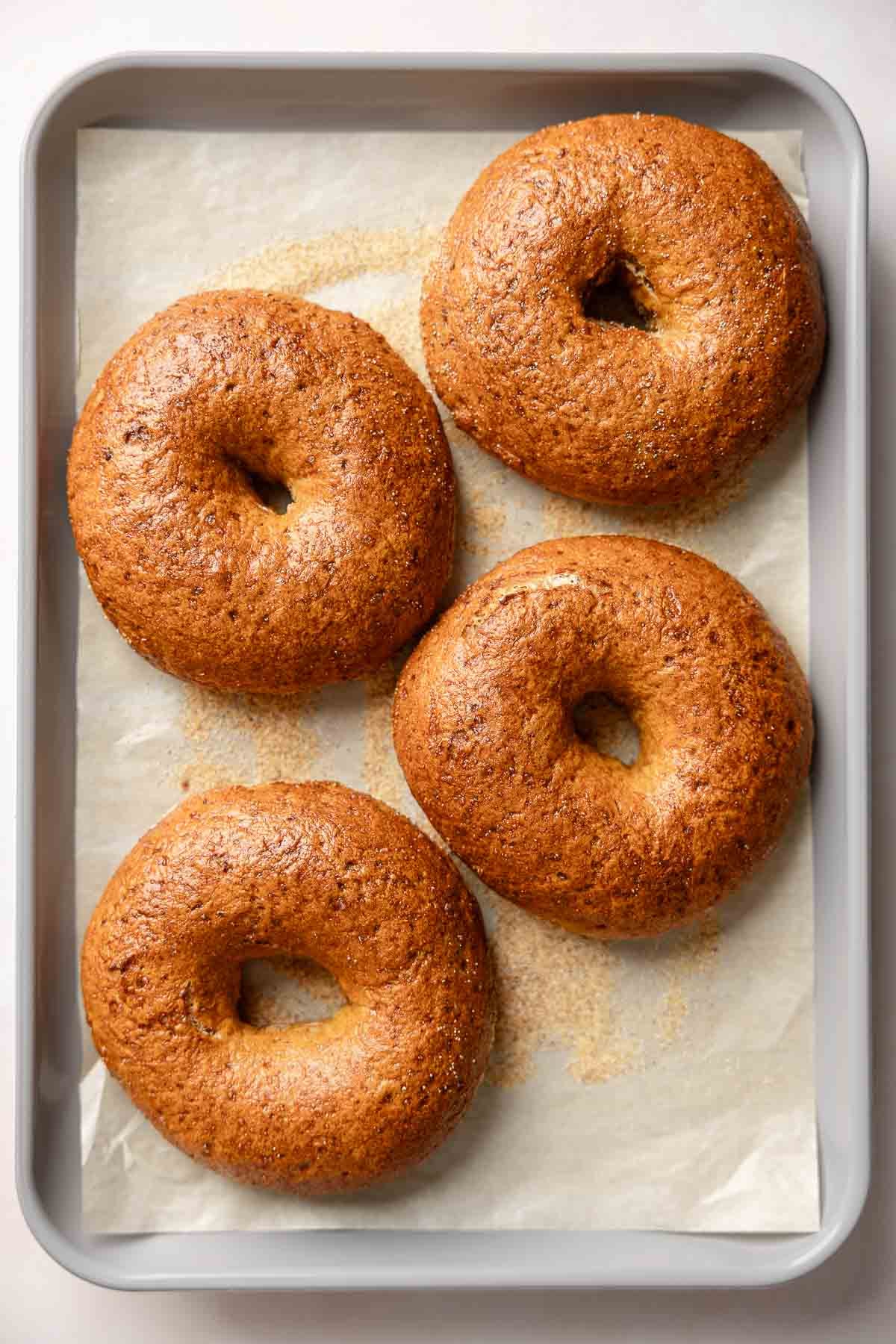 Four baked gluten-free pumpkin bagels with glossy, golden-brown crusts on a parchment-lined baking sheet.