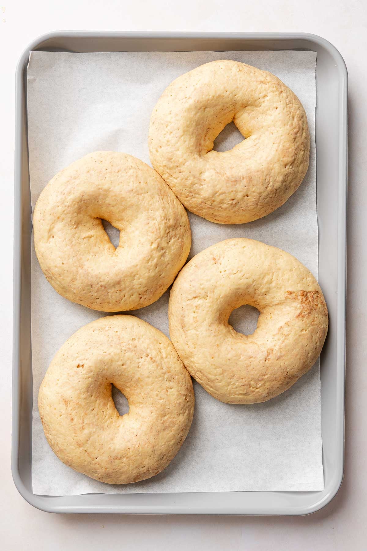 Four puffy gluten-free pumpkin bagels after rising, with noticeably smaller center holes.