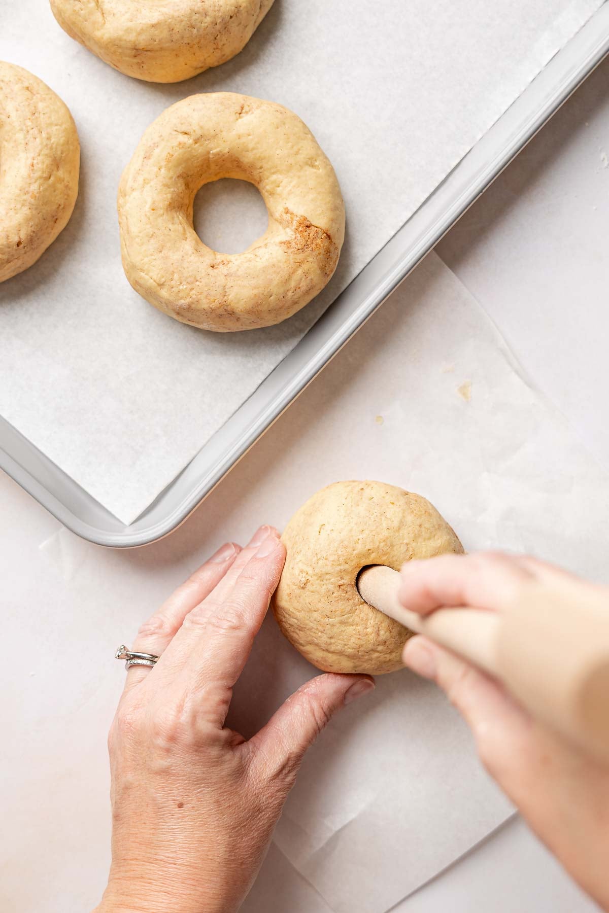 Using a wooden utensil handle to poke a hole through the center of gluten-free pumpkin bagel dough.