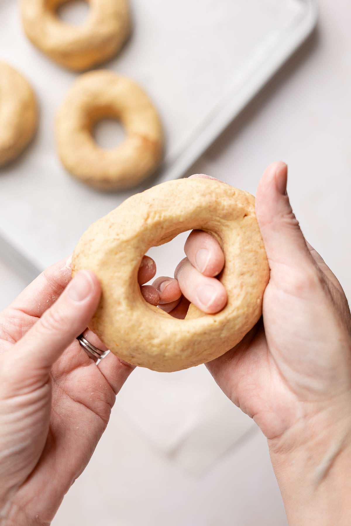 Gently stretching the center hole of a gluten-free pumpkin bagel with both hands.